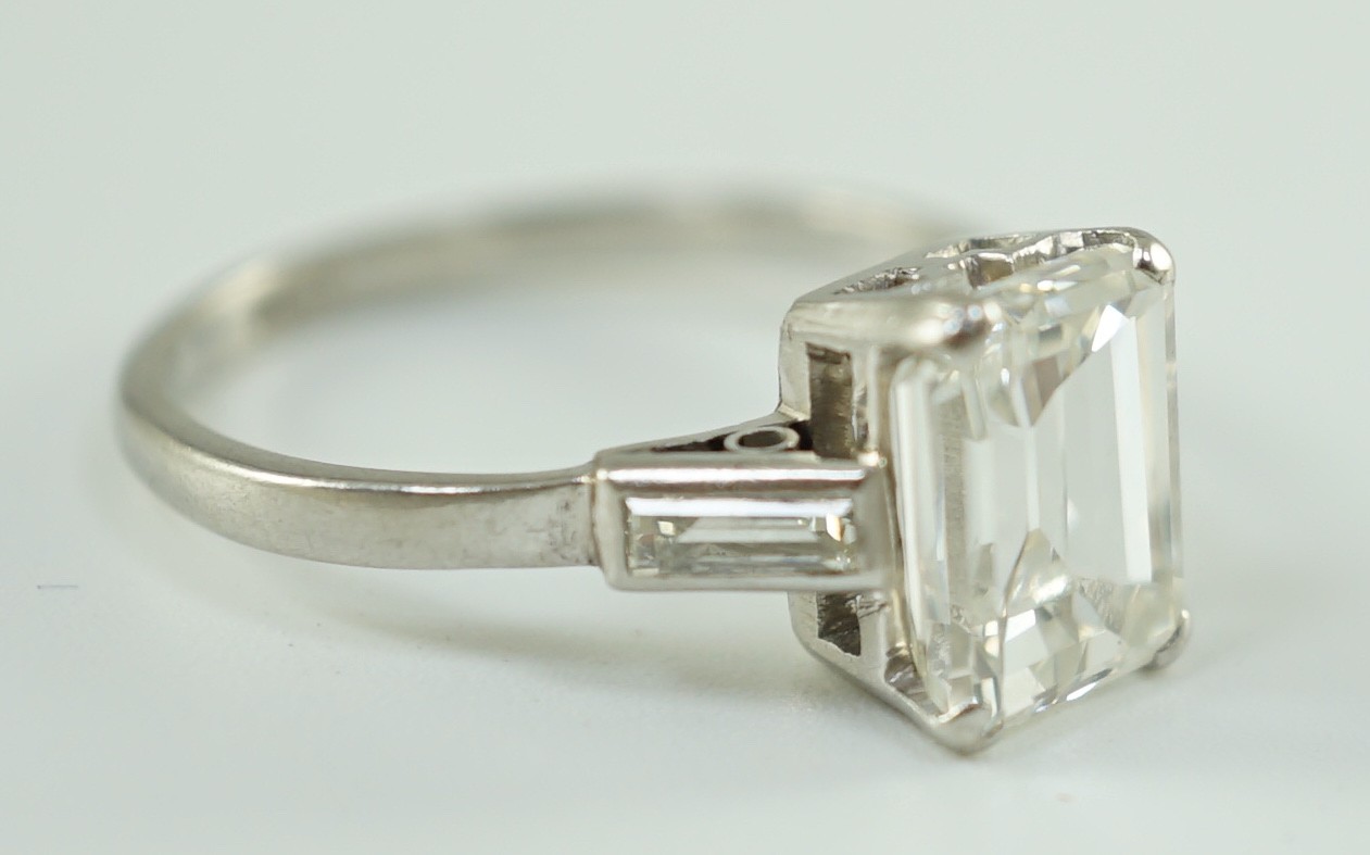 A platinum and single stone emerald cut diamond set ring, with baguette cut diamond set shoulders